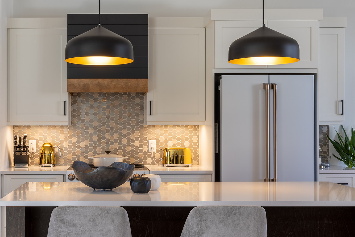 A modern kitchen with white cabinetry, a hexagonal tile backsplash, sleek stainless steel appliances, and a central island with decorative bowls and contemporary pendant lighting.