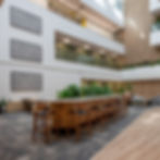 Modern atrium with custom bar-height table, green plants, and abstract wall art. Bright lighting and light wood accents create a calm ambiance.