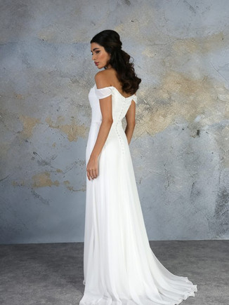 This off the shoulder dress has a beautifully draped neckline, which flows into the flattering floor length chiffon skirt. The soft train floats effortlessly from the waist to add softness to the look.