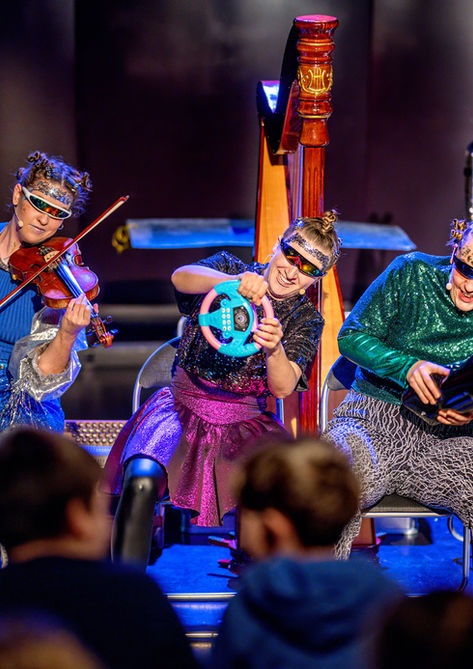 Vier Musikerinnen in futuristischen Glitzerkostümen mit Geige und Harfe bei einer interaktiven Bühnenperformance vor Publikum - Projekt 5fürEva