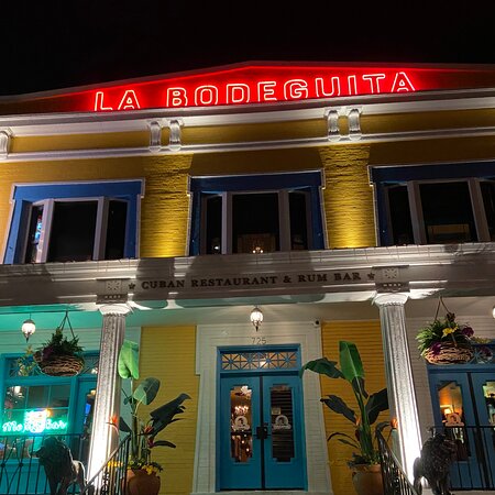  The vibrant yellow exterior of La Bodeguita De Mima Cuban restaurant in Louisville, Kentucky, featuring tropical décor and a large cigar sign.