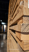 A pile of raw oak wood staves stacked against a historic red brick wall under a black industrial beam at Old Forester.
