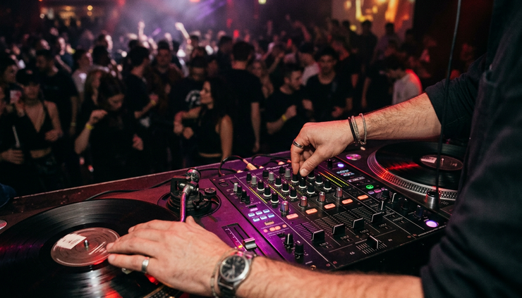 Close-up view of a DJ mixer with hands adjusting knobs under red club lights