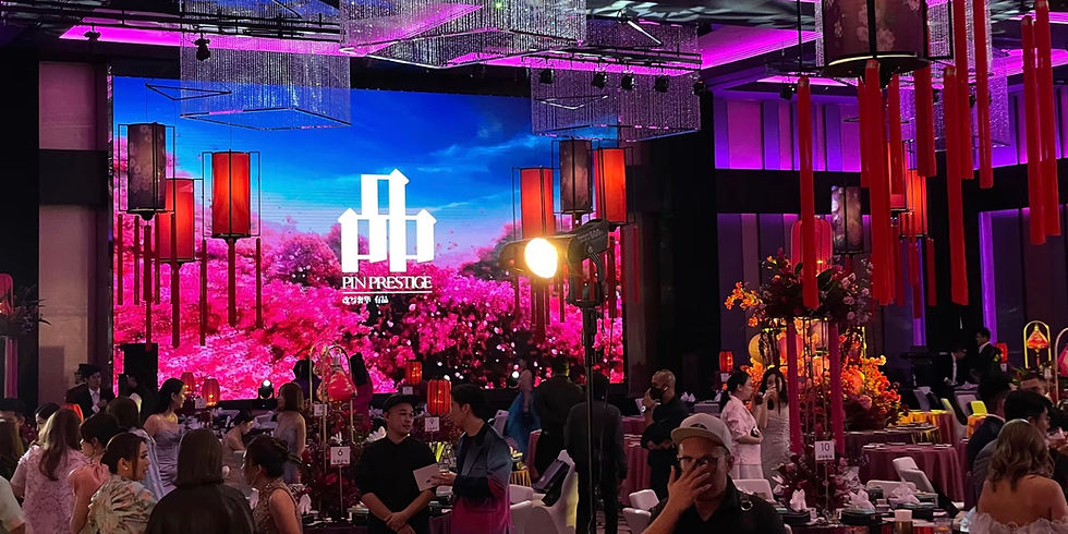 Guests mingling at gala dinner with magenta-lit ceiling, crystal chandeliers, and LED video wall displaying brand visuals.