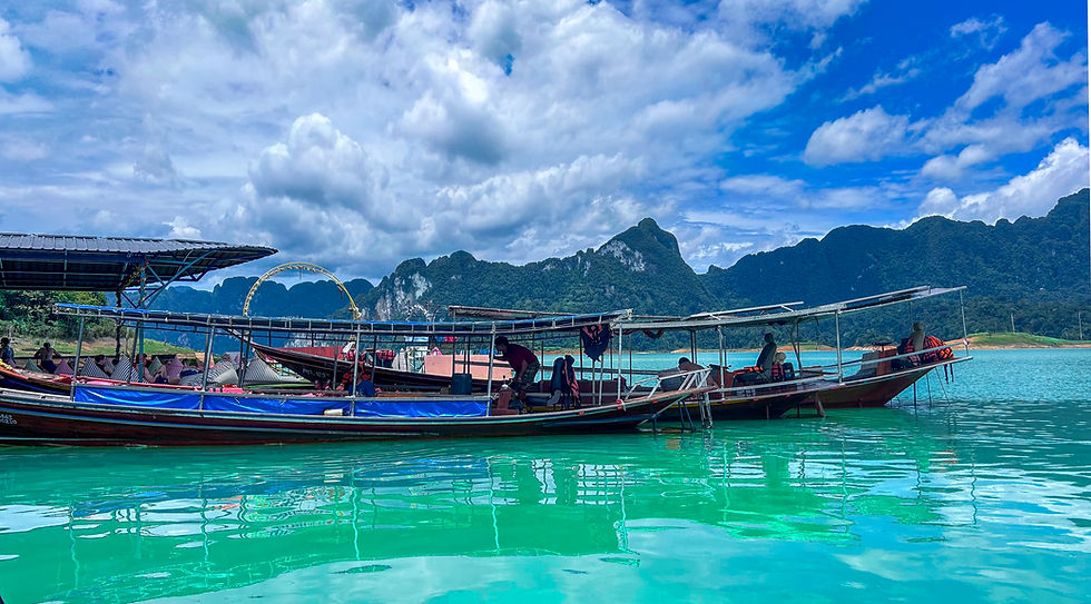 Longboats with tourists on turquoise water under dramatic clouds, backed by forested limestone mountains, serene tropical scene in Thailand.