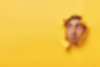 face-surprised-scared-young-man-gazes-through-yellow-paper-hole-aside-sees-something-shock