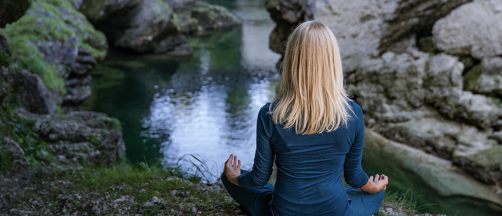 Doris Speigner meditiert mit erhobenen Händen an einem Bach in der Natur.
