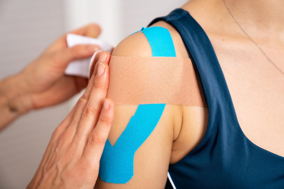 A person is precisely applying a beige adhesive bandage over blue kinesiology tape on anothers shoulder, captured in detail by NW Photography. The subject, in a navy tank top, emphasizes the professionalism and expertise of corporate photography services focused on health and wellness.