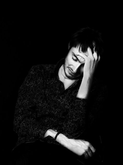A black and white image captures a person sitting with their head resting on one hand, eyes closed, appearing contemplative or weary, against a dark background—an evocative masterpiece in professional portrait photography by NW Photography.