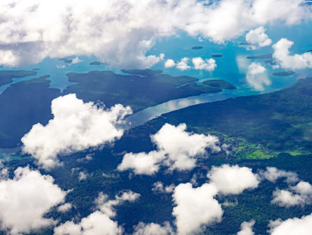 Aerial view of Raja Ampats lush, forested landscape with a winding river embraced by clouds. Small patches of greenery and water bodies dot the scene below, creating a serene and expansive divers paradise—a true gem for any travel blog.