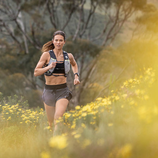 Female trail runner mid-stride in wildflowers during a sports photography shoot on a Cape Town trail