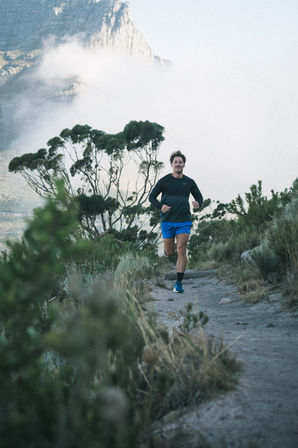 Trail runner photographed on Cape Town mountain path with expansive green landscape and sky background – professional trail running photographer Cape Town