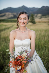 Bride smiling with colorful summer bouquet in front of the mountains at sunset