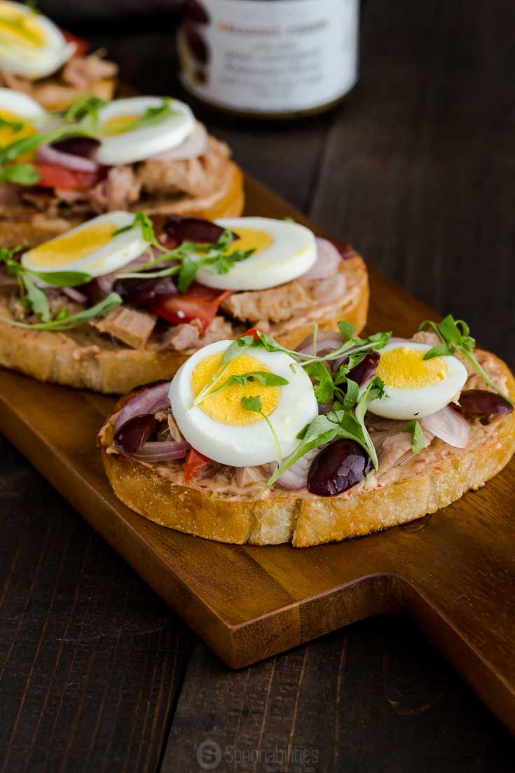 Close up shot of nicoise toasts with hardboiled egg and Kalamata Olives on a wood board