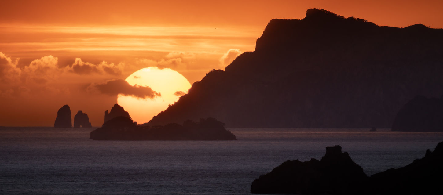 Sunset with the sun behind Capri and its faraglioni seastacks
