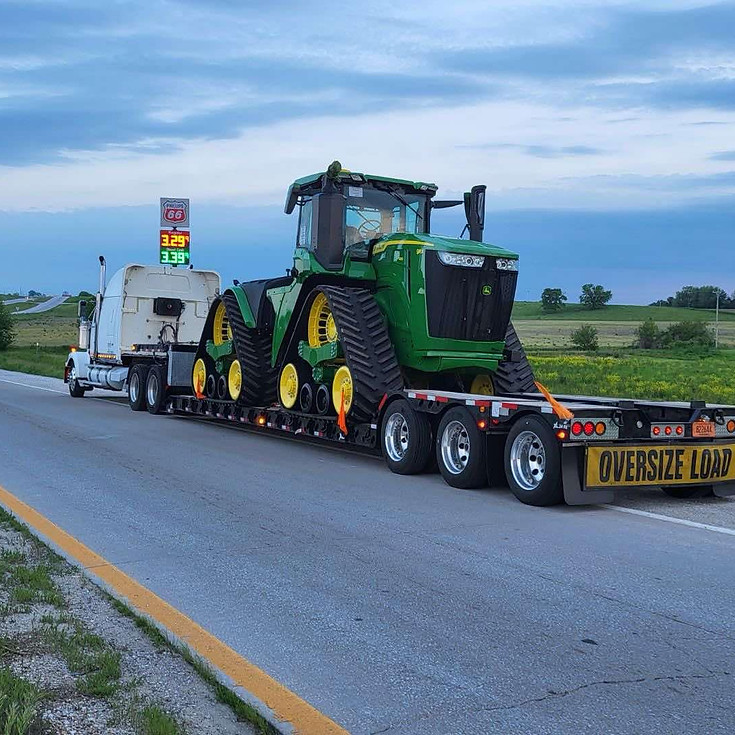 White semi hauling a John Deere tractor on a double dropdeck trailer.