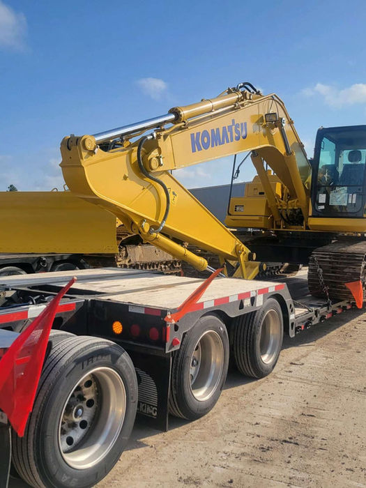 Excavator being hauled by a white semi on a double drop trailer.
