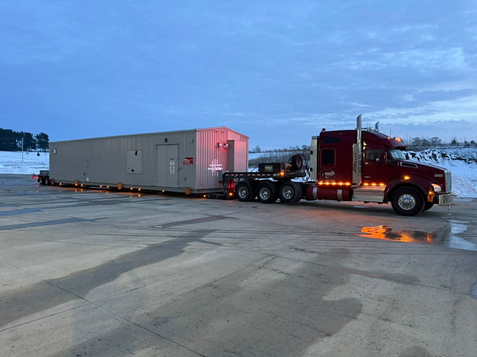 Maroon semi hauling an enclosure building.