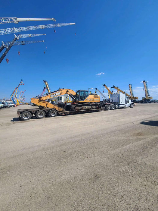 Caterpillar excavator being hauled by a white semi on a double drop trailer. 