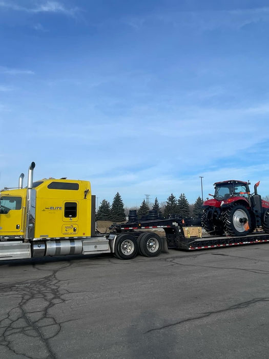 Yellow semi hauling a tractor on a double drop trailer.