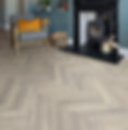 Cozy room with herringbone LVT floor, gray chair with orange pillow, fireplace, and teal cabinet. Candles and a basket add warmth.