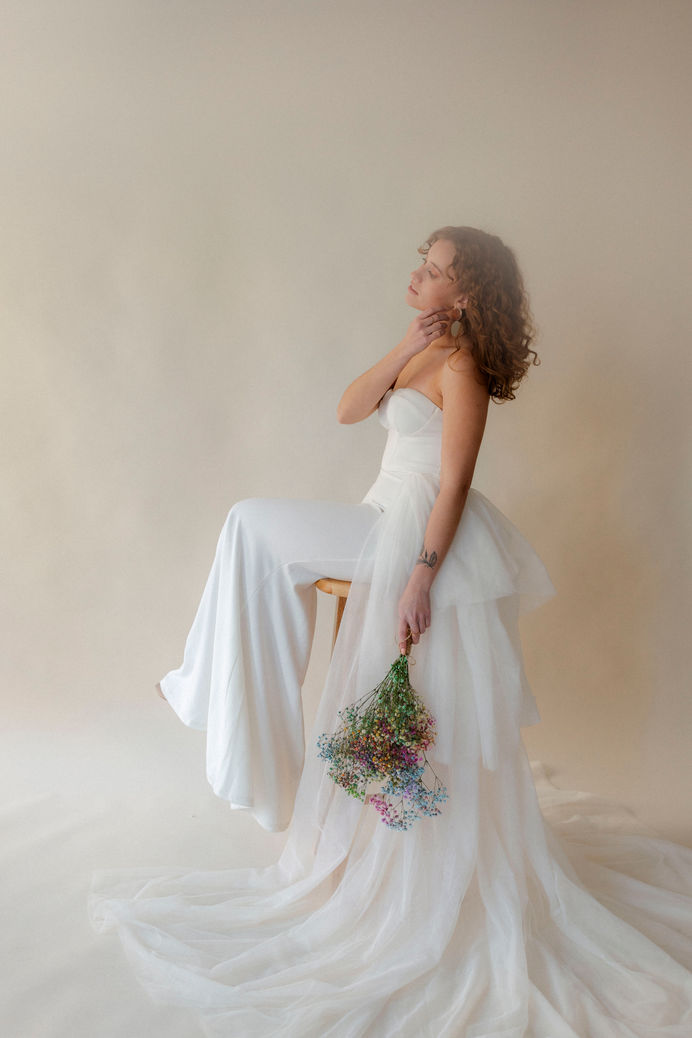 Bridal portrait sitting on a stool in studio, holding bouquet with layered tulle train cascading around.