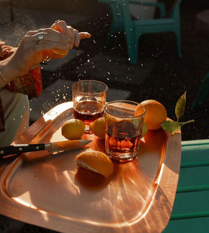 Hands squeezing an orange for a classic cocktail, shot with film wedding photographer style, editorial and candid feel.