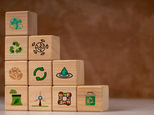 Blocos de madeira empilhados com ícones de sustentabilidade, acessibilidade, economia circular, água limpa, reciclagem e inclusão, representando a contribuição do design para os ODS.