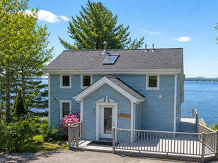The frontside exterior of Baycliff Cottage, surrounded by trees and a spacious wraparound deck.