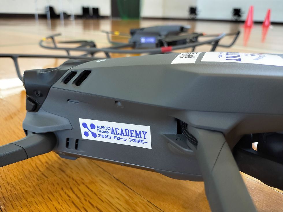 教室の床に置かれたドローンのクローズアップ。ドローンには「ALPICO Drone ACADEMY」のラベルが貼られている。背景にオレンジのコーン。ドローンクロスがジュニアドローン教室を開催。
