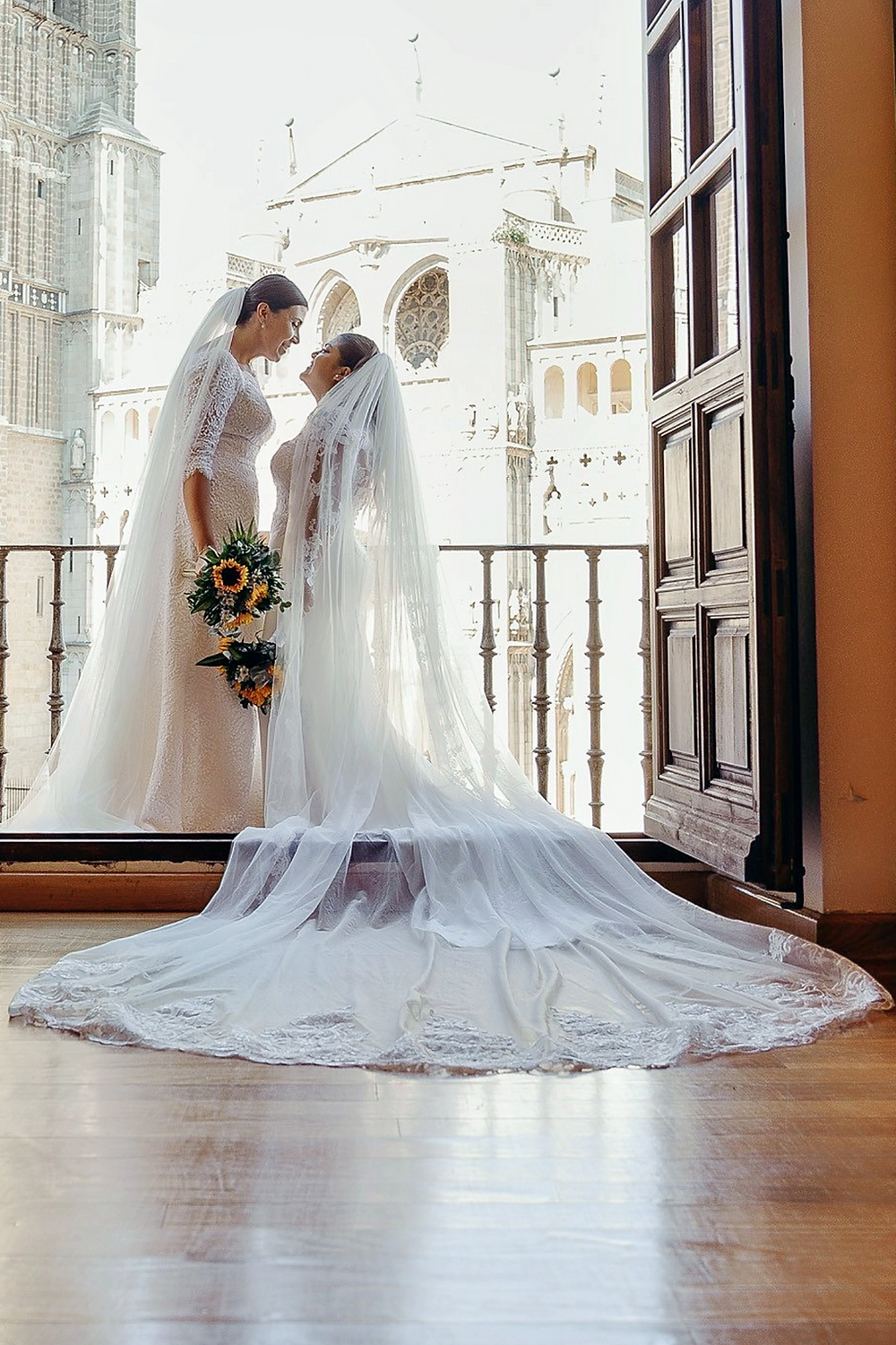 Dos novias en balcón con catedral de fondo en Toledo.