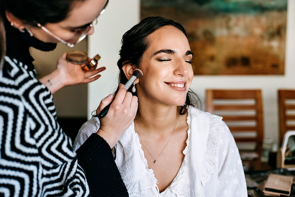 Maquillador aplicando rubor a Irene, la novia sonriente.