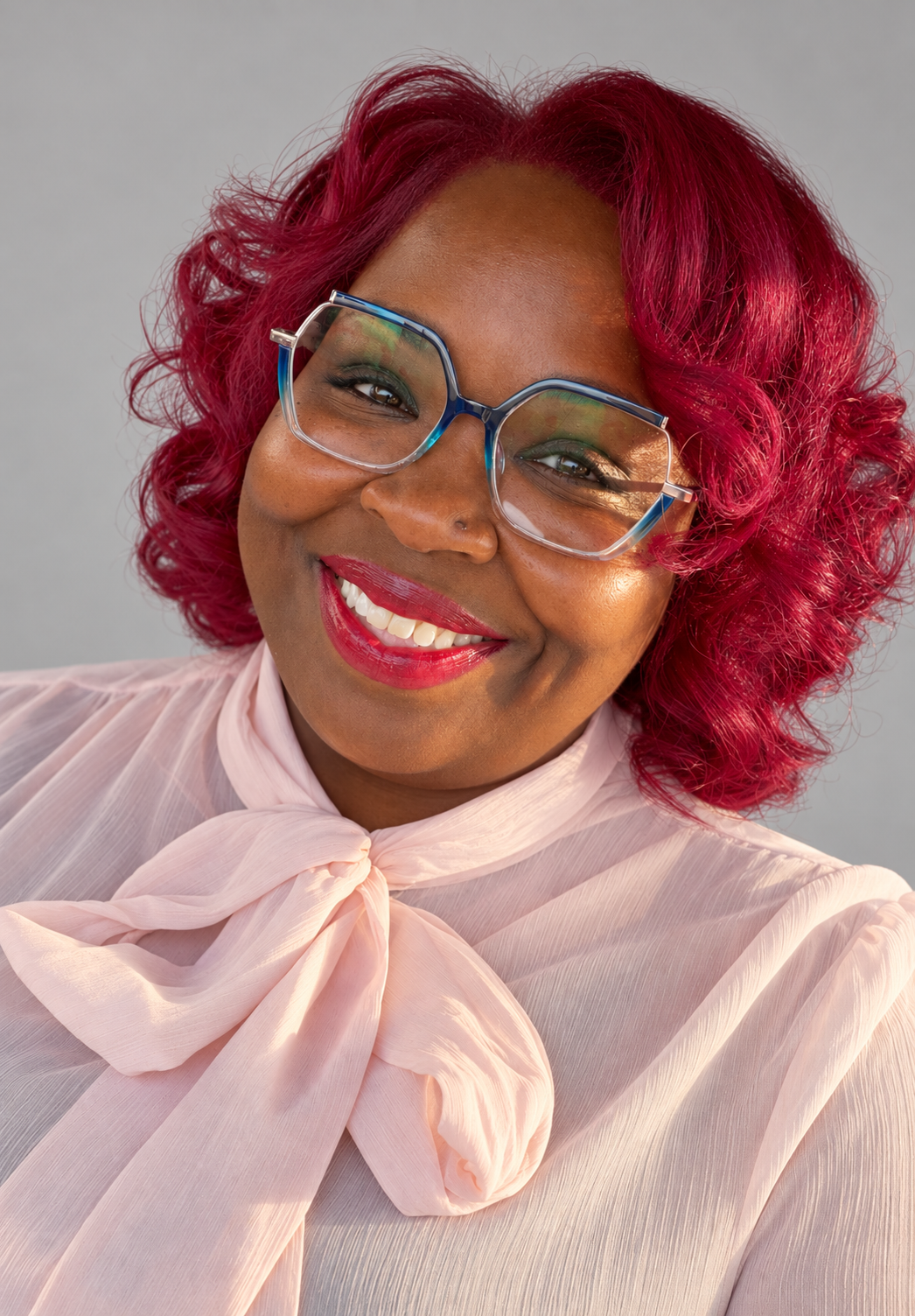 Portrait of Diana Johnson smiling, wearing a blush bow blouse and blue glasses