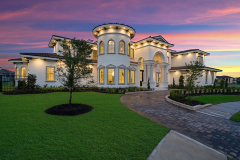 Luxury twilight photo of a Mediterranean-style mansion illuminated with elegant exterior lighting under a stunning pink and purple dusk sky. Captures architectural elegance and evening ambiance in perfect harmony. Captured by Strata Visuals.