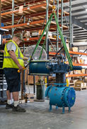 Technician operating a heavy-duty valve system inside a warehouse, wearing a safety vest and using lifting straps to position industrial machinery — captured by Strata Visuals for business and commercial photography.
