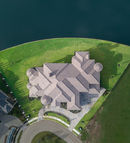 Drone top-down view of a luxurious lakeside mansion with a circular driveway, manicured lawn, and surrounding calm waters. Captured by Strata Visuals.