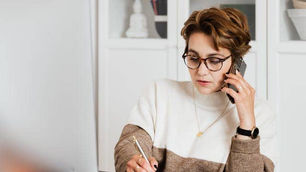 Women is sitting at desk using phone with computer open.