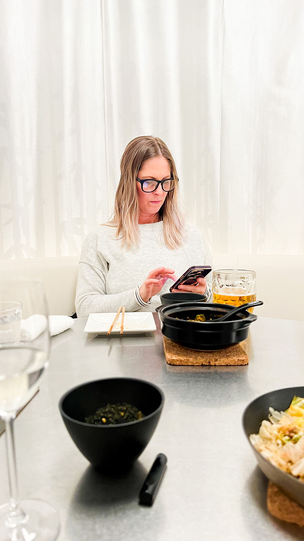 a blonde woman works on her phone while sitting in a restaurant