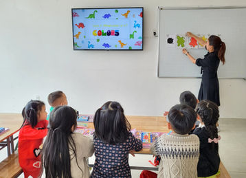 Cô giáo dạy học sinh, chữ COLORS trên màn hình, trong lớp học.