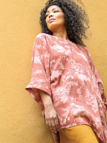 Model wearing Pink Floral Sleeve Poncho leaning against a Mustard-coloured wall.