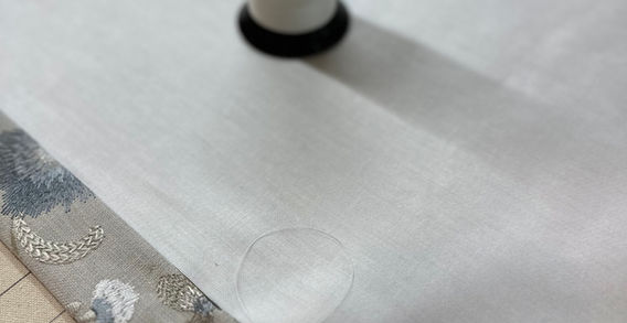 Neutral fabric and spool of thread on Rideaux Designs workroom table during custom soft goods fabrication