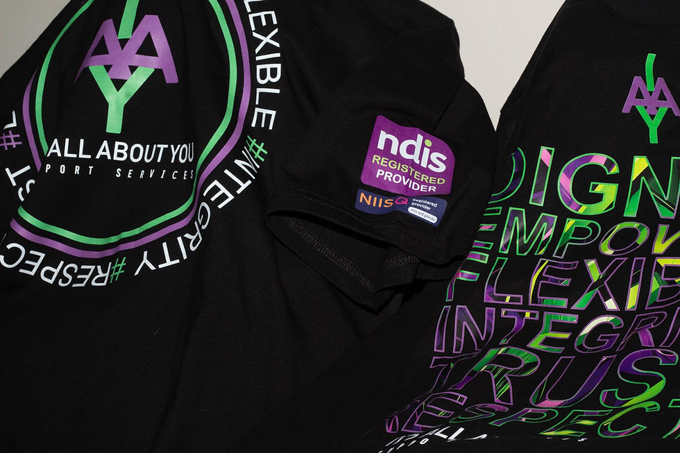 Black shirts featuring colorful text and logos, including "All About You" and "NDIS Registered Provider." Emphasizes empowerment and flexibility.