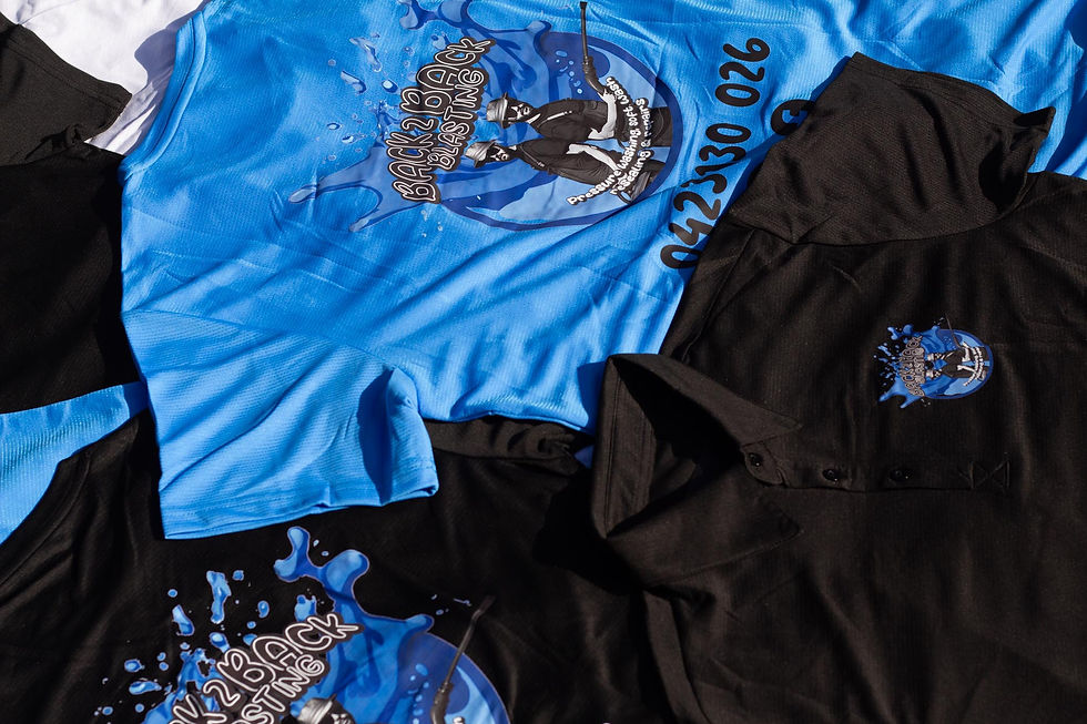 Blue and black shirts with "Back 2 Back Blasting" logo and text displayed, featuring a cartoon graphic and phone number. Laid on white fabric.