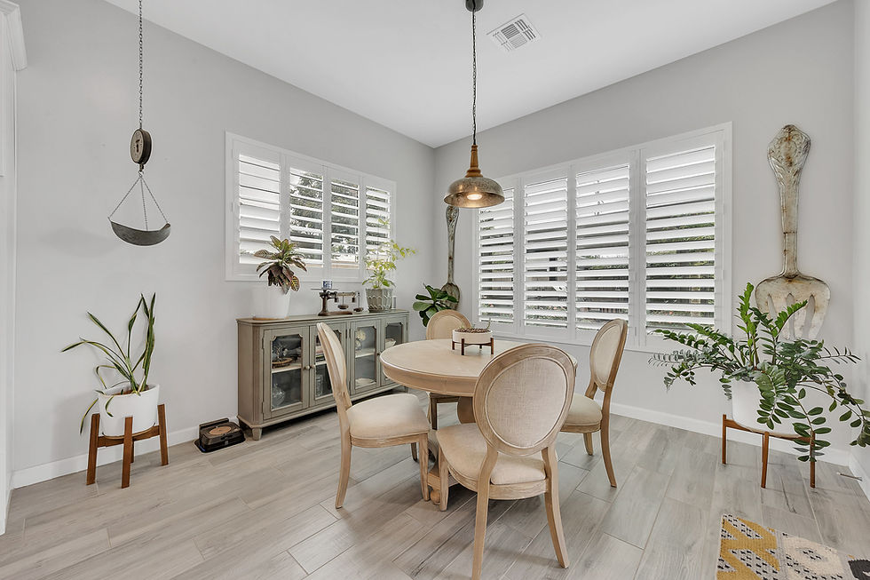 Bright dining room with round table, chairs, plants, and window shutters