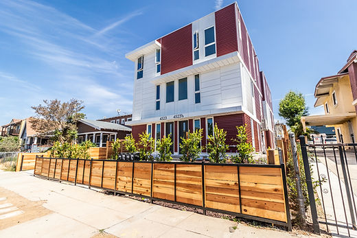 multifamily home with red detailing and a wooden fence with landscaping