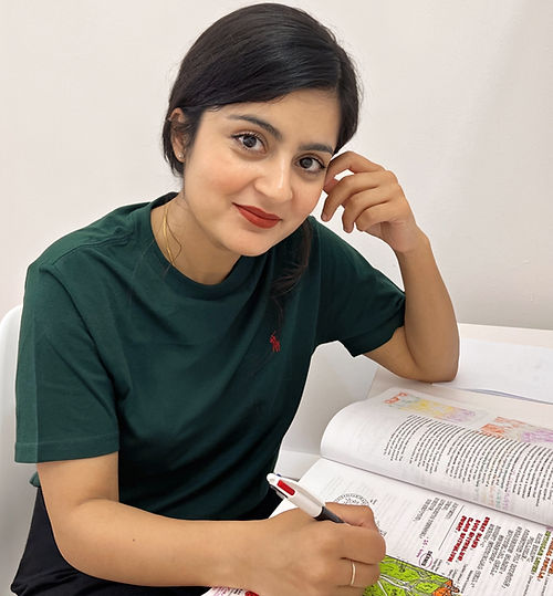 Picture of Dermic Clinic CEO, Dr Ambreen Mirza, wearing a green top, holding a pen with a book open and looking at the camera.