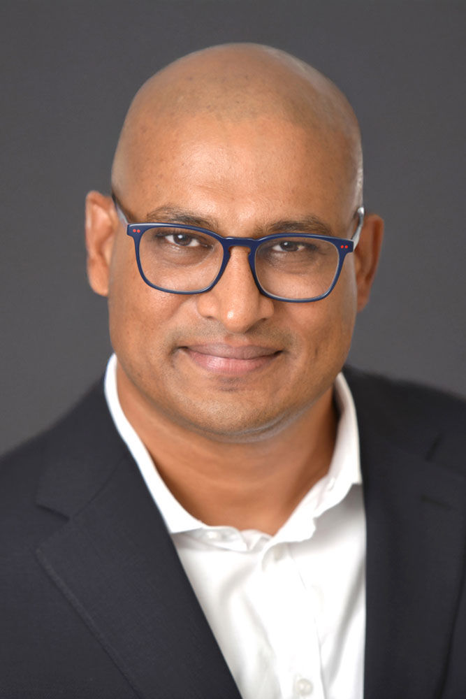 Bald man with blue glasses smiling for studio portrait