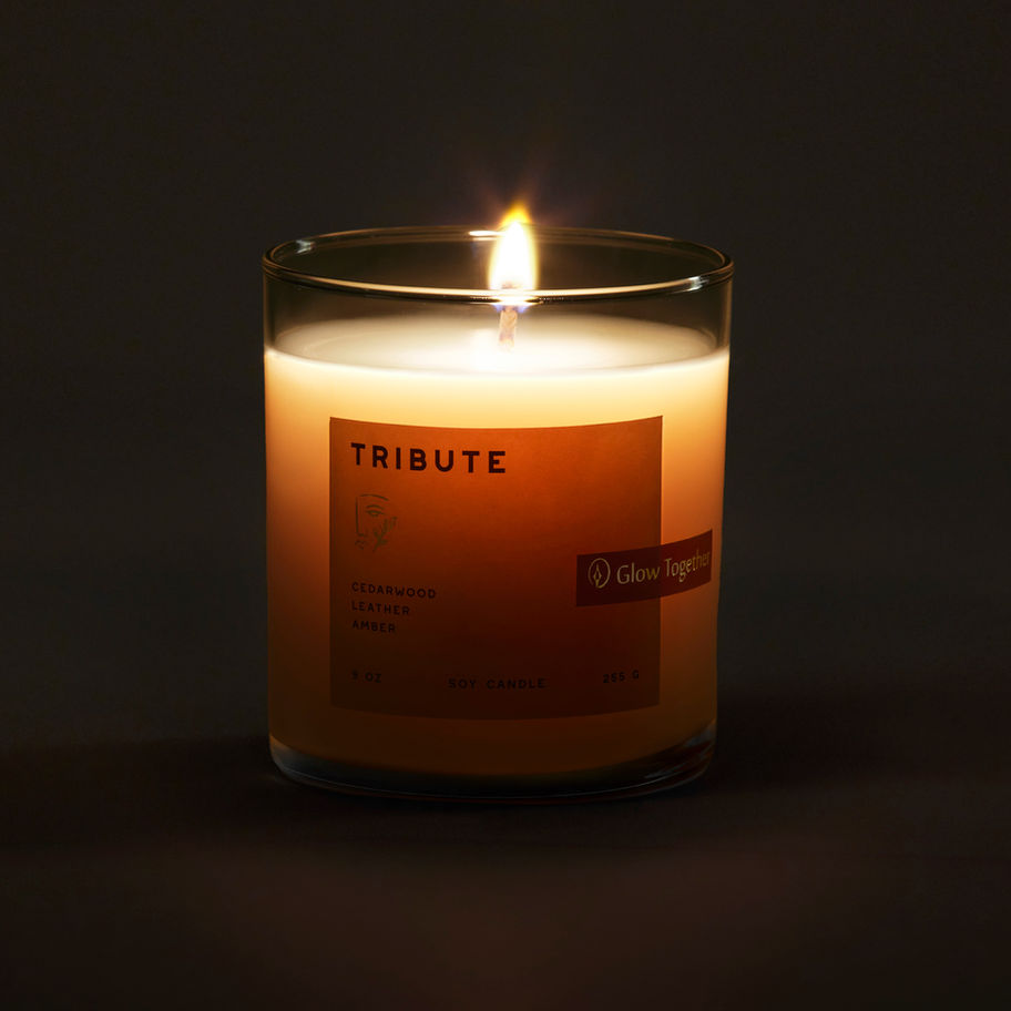 Lit Tribute candle glowing with a soft warm flame in a dark setting
