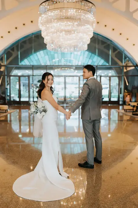 Bride and groom holding hands under a large chandelier.
