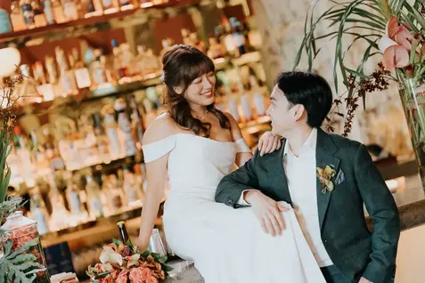 Bride and groom smiling at each other at a bar.